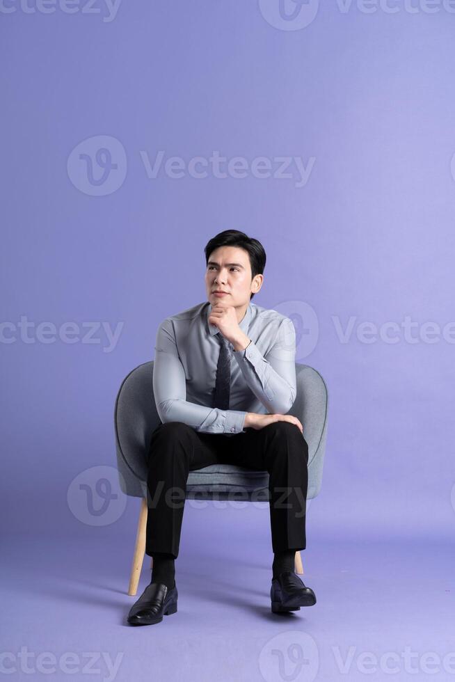 Portrait of Asian business man sitting on sofa, isolated on purple background photo