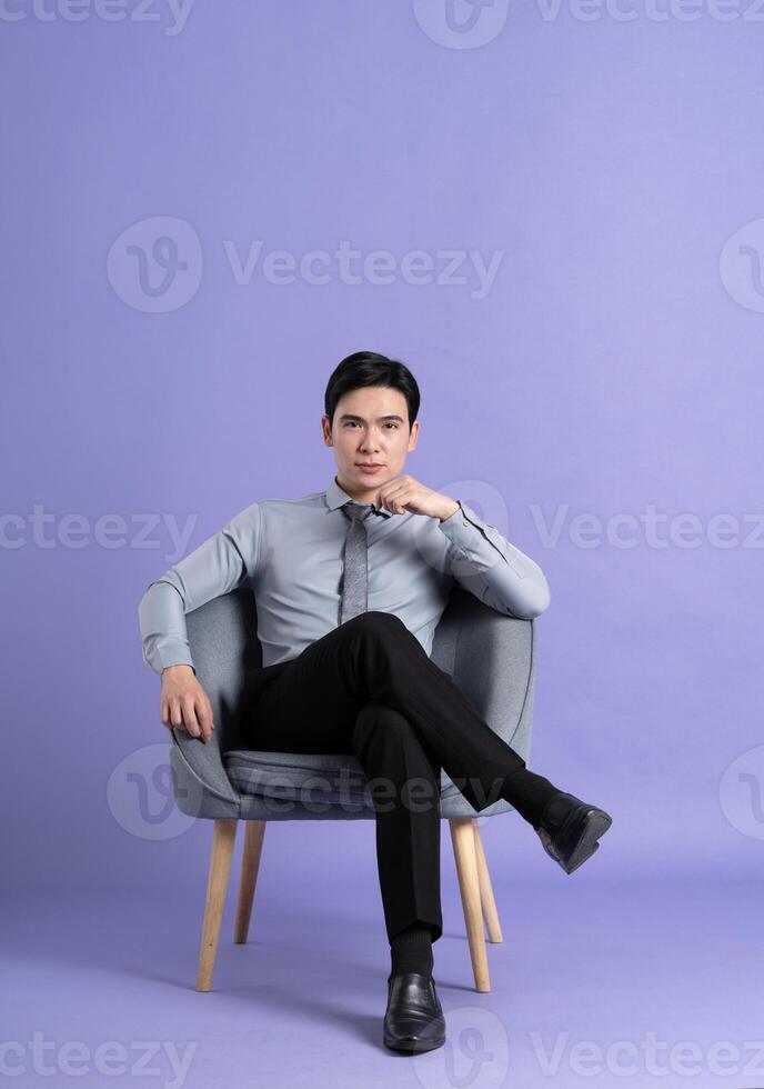 Portrait of Asian business man sitting on sofa, isolated on purple background photo