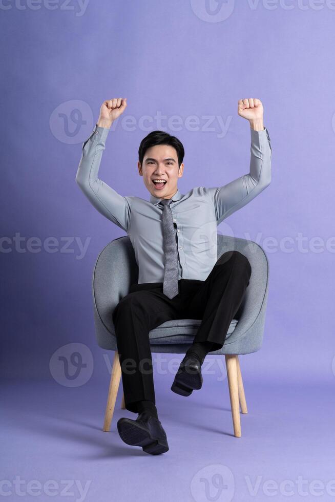 Portrait of Asian business man sitting on sofa, isolated on purple background photo