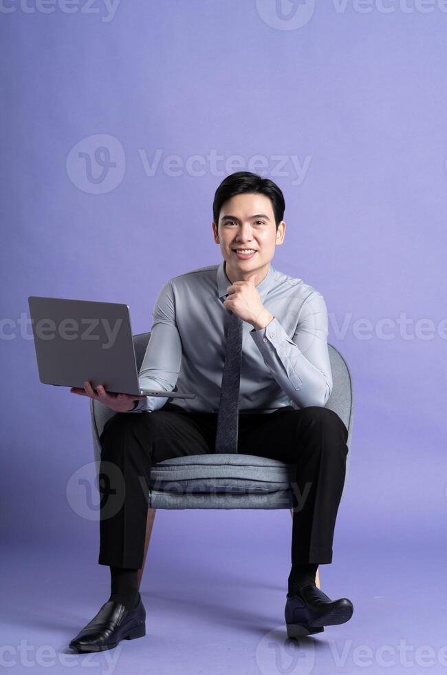 Portrait of Asian business man sitting on sofa, isolated on purple background photo