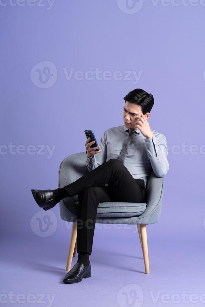 retrato de asiático negocio hombre sentado en sofá, aislado en púrpura antecedentes foto