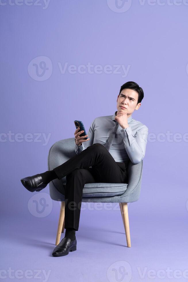 Portrait of Asian business man sitting on sofa, isolated on purple background photo