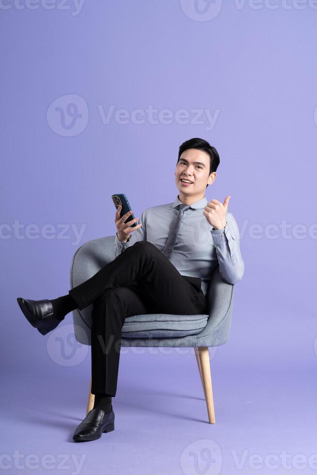 Portrait of Asian business man sitting on sofa, isolated on purple background photo