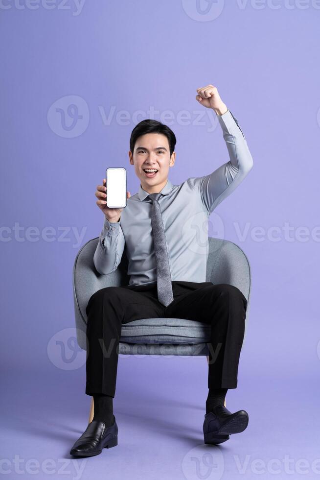 Portrait of Asian business man sitting on sofa, isolated on purple background photo