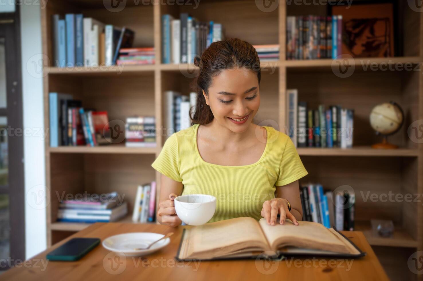 Young woman reading book and drink hot coffee in library at home, smiling, laughing, enjoying bookworms hobby, home leisure time photo