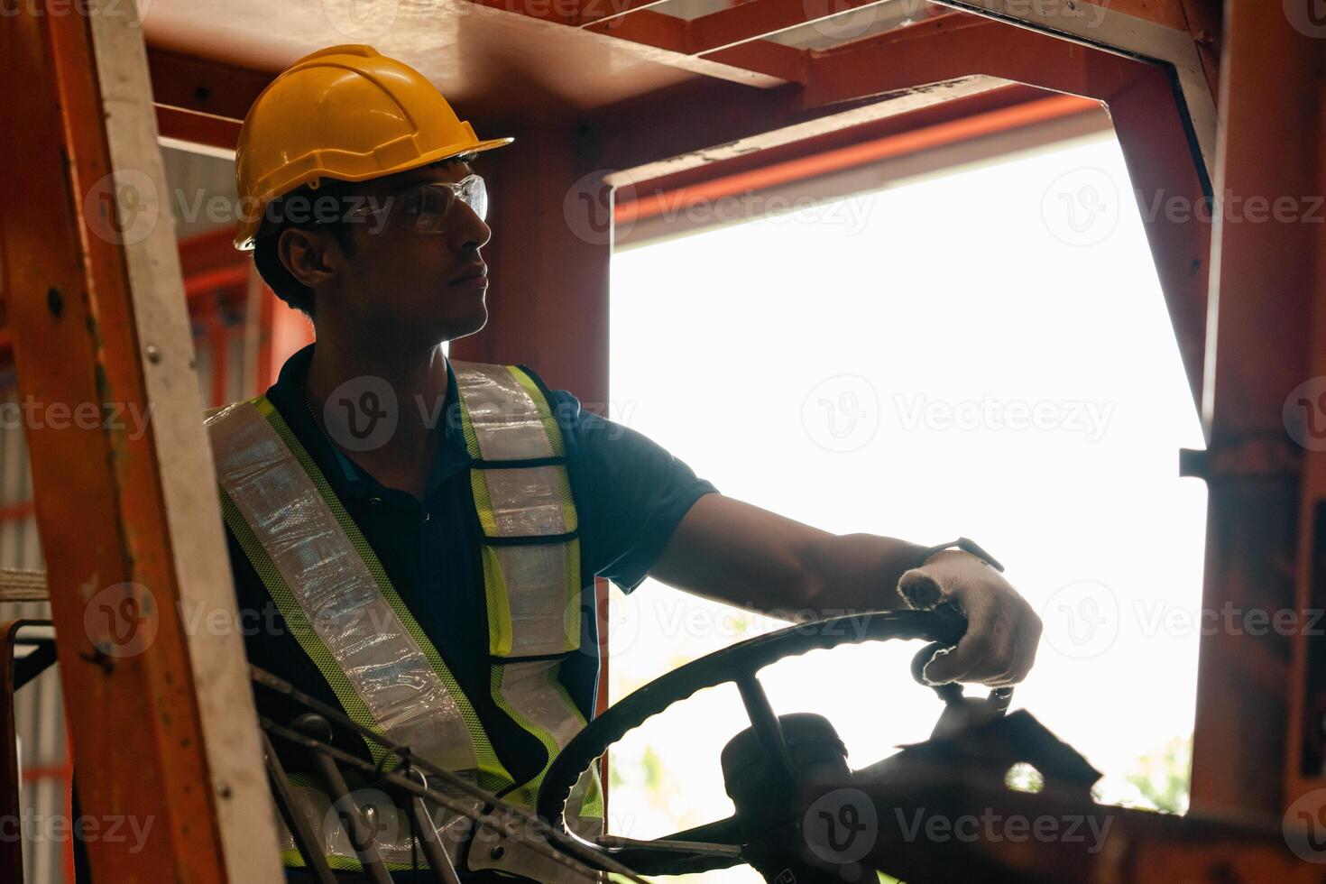 un masculino máquina elevadora conductor enfocado en cuidadosamente transportar valores desde estantería alrededor el piso de un grande depósito. foto