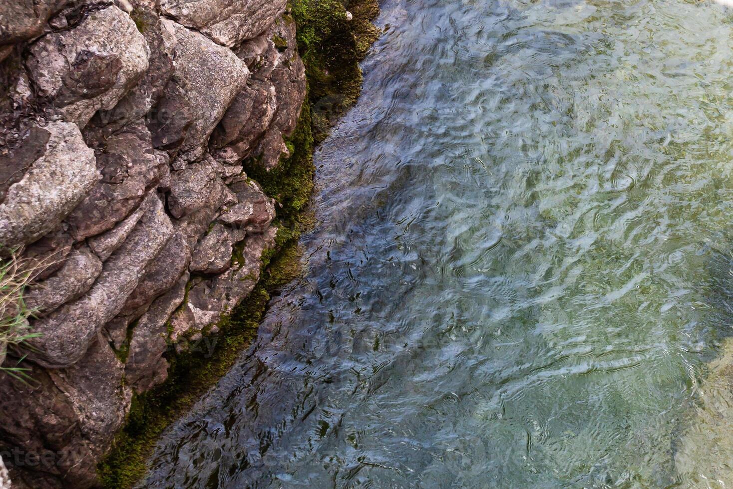 River flowing along a rocky cliff next to a waterfall, with moss and reflections in the water. View from above. Background. Texture. Horizontal. photo