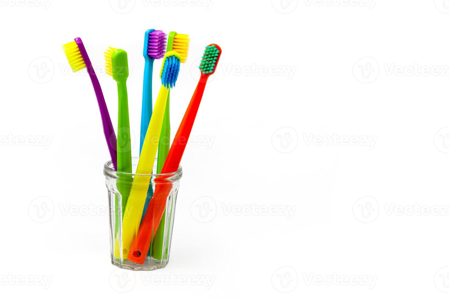 Three toothbrushes - purple, orange and yellow with different colored bristles in a clear cup on a white background. Insulated. Vertical. Photo in high quality.