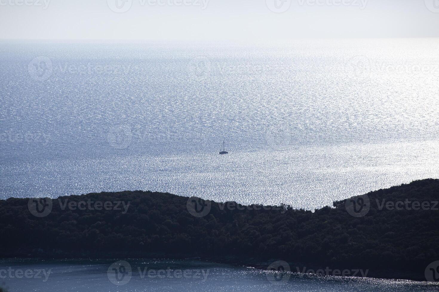 A small sailing ship sailing along the sea surface of the Adriatic Sea. An island with green trees. View from above. Montenegro. Budva. Horizontal. photo