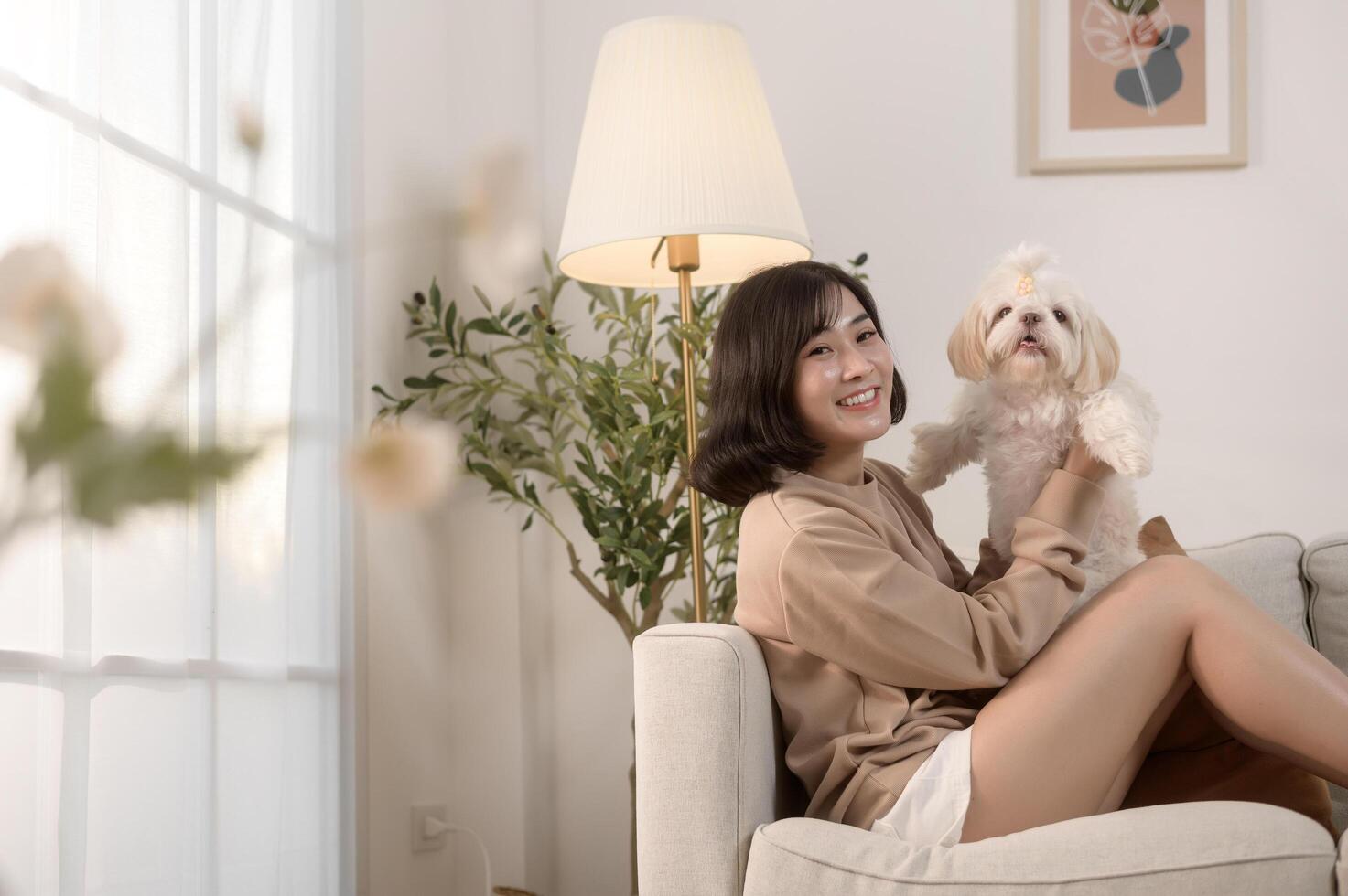 Happy young asian woman cuddling and spending time with cute dog in living room. photo