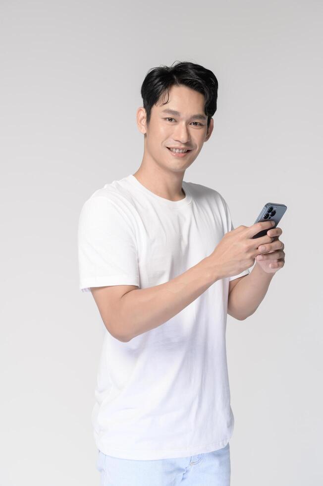 Portrait of young smiling asian man using smartphone over white background photo