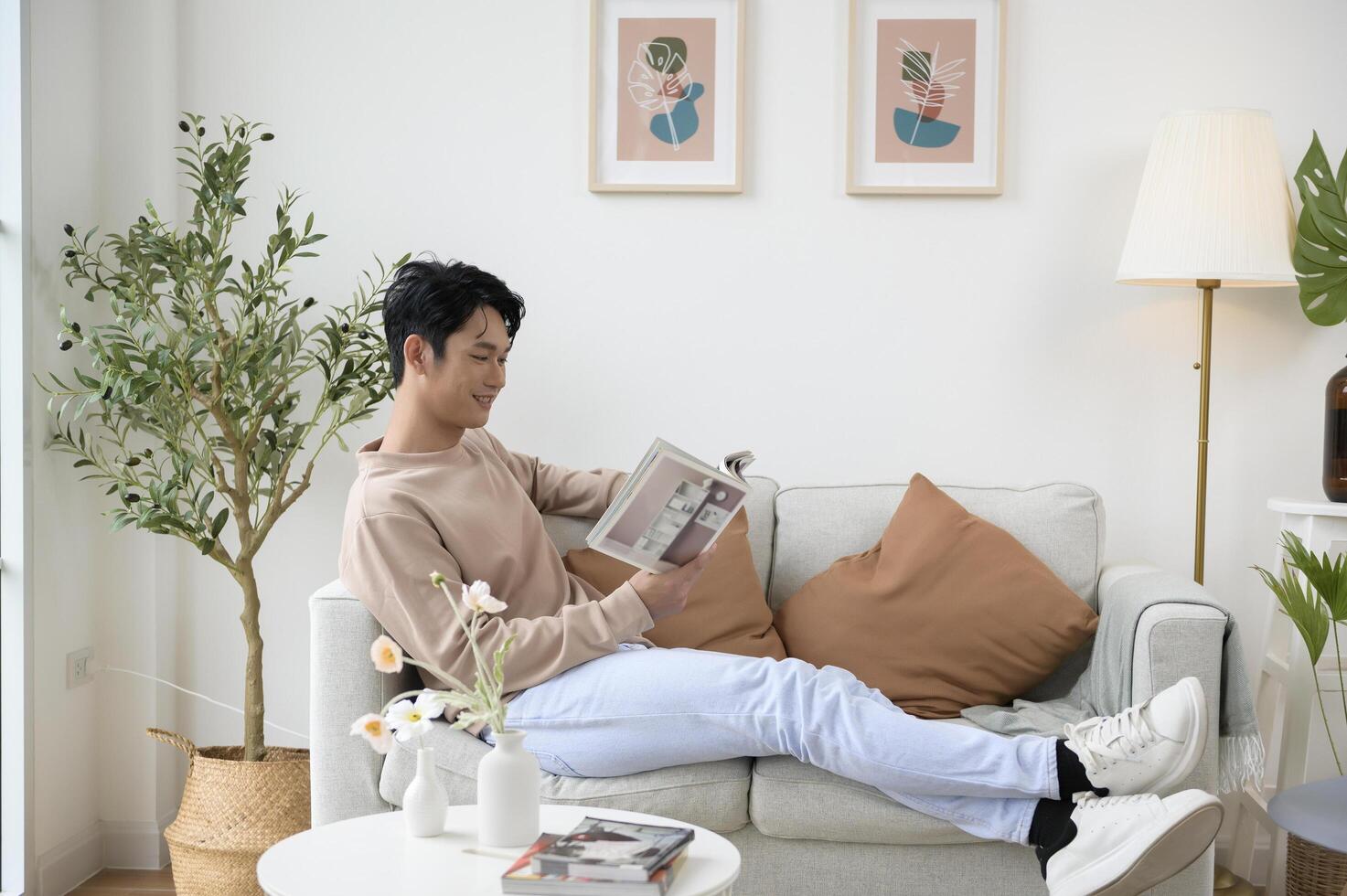 Happy asian man sitting on couch  reading a book in living room at home, relax time and lifestyle concept photo