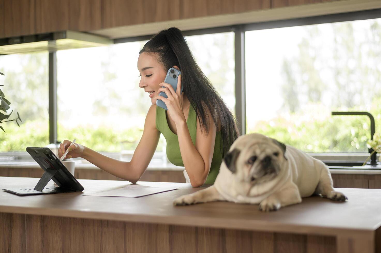 joven asiático mujer trabajando con tableta y disfrutando con su perro en el cocina a hogar foto