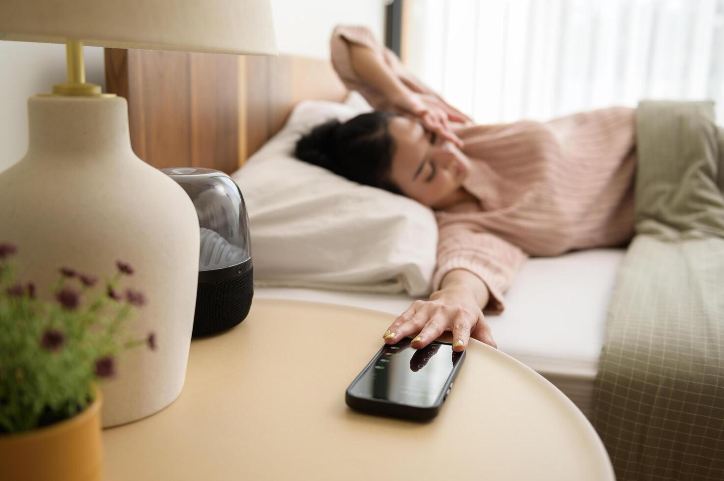 Sleeping asian woman turning off alarm on smartphone while being Waken up in the morning photo