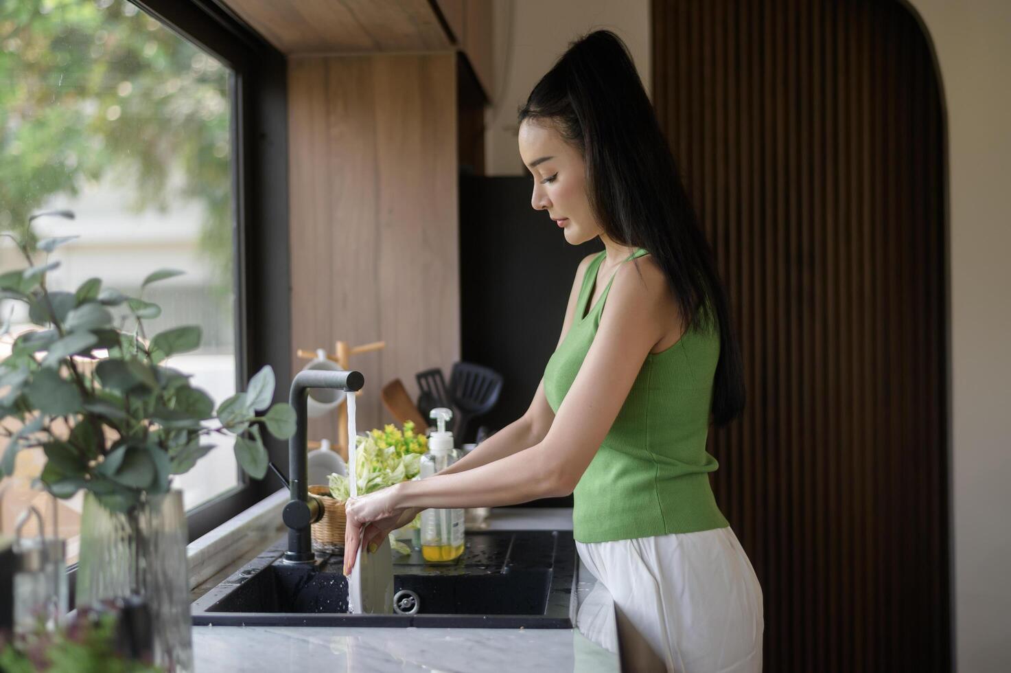 asiático mujer Lavado platos en el cocina lavabo a hogar foto