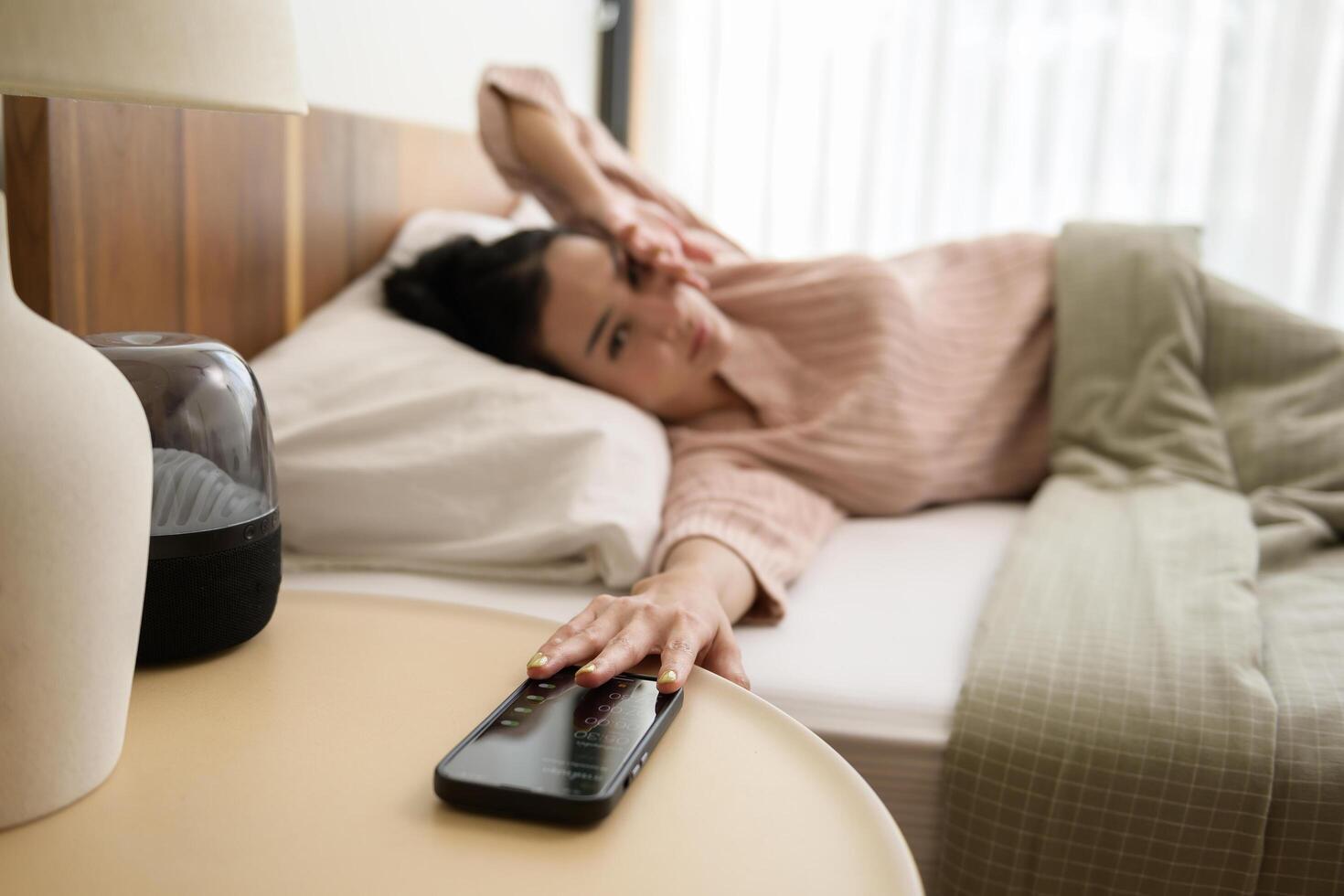 dormido asiático mujer torneado apagado alarma en teléfono inteligente mientras siendo despertar arriba en el Mañana foto