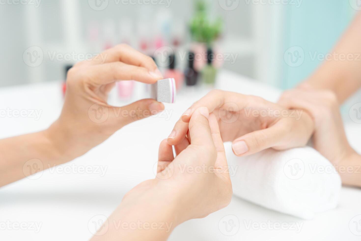 la mujer recibe el servicio de atención de la manicura esteticista profesional en el centro de spa. el salón de belleza de uñas usa una lima de uñas para el tratamiento de acristalamiento. manicurista hace que el cliente de uñas sea hermoso. tratamiento de spa para el cuidado del cuerpo foto