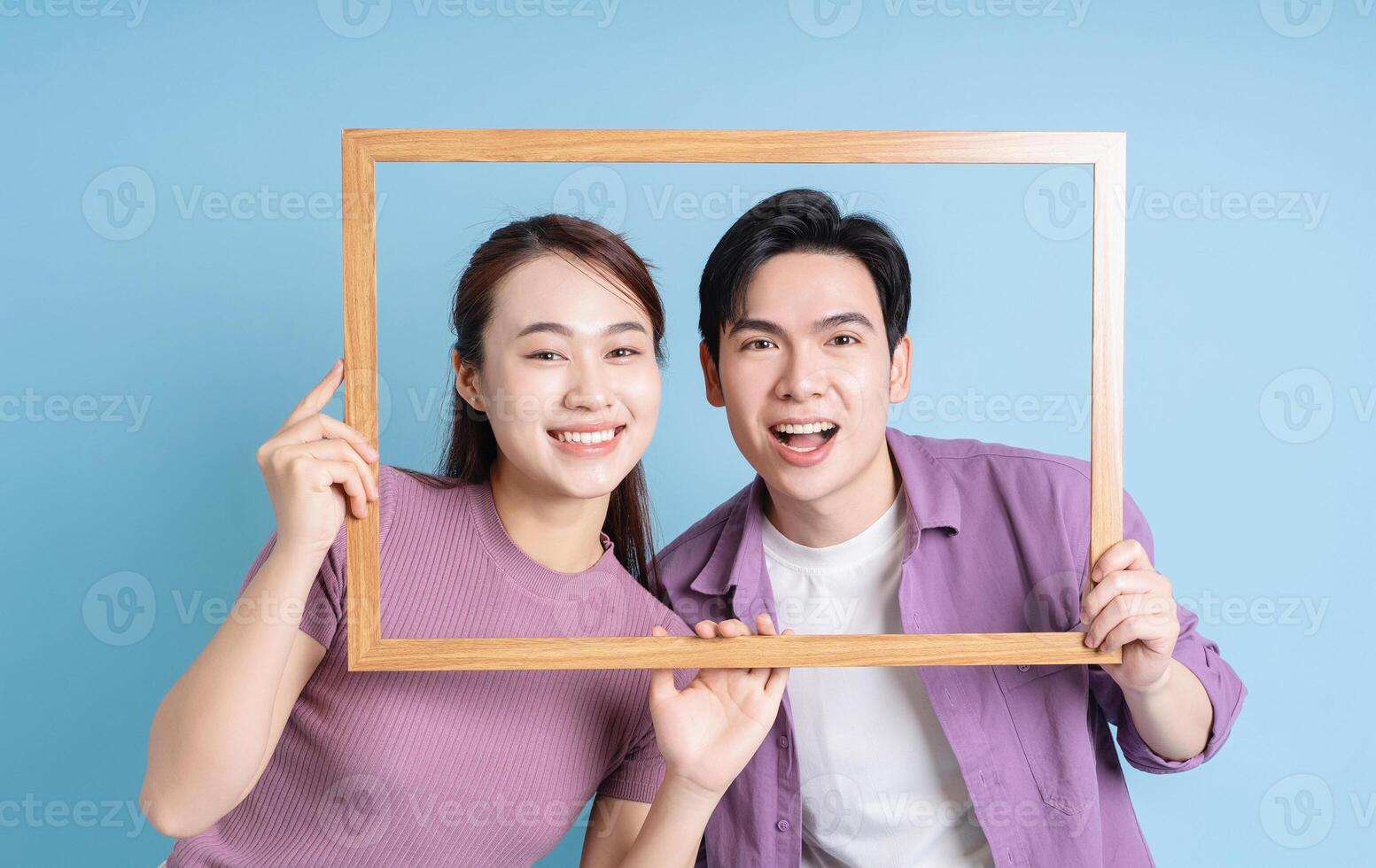 Young Asian couple holding photo frame on blue background