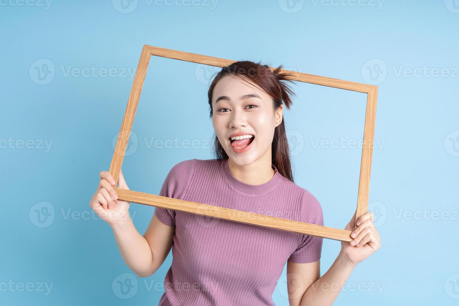 Young Asian woman holding photo frame on blue background