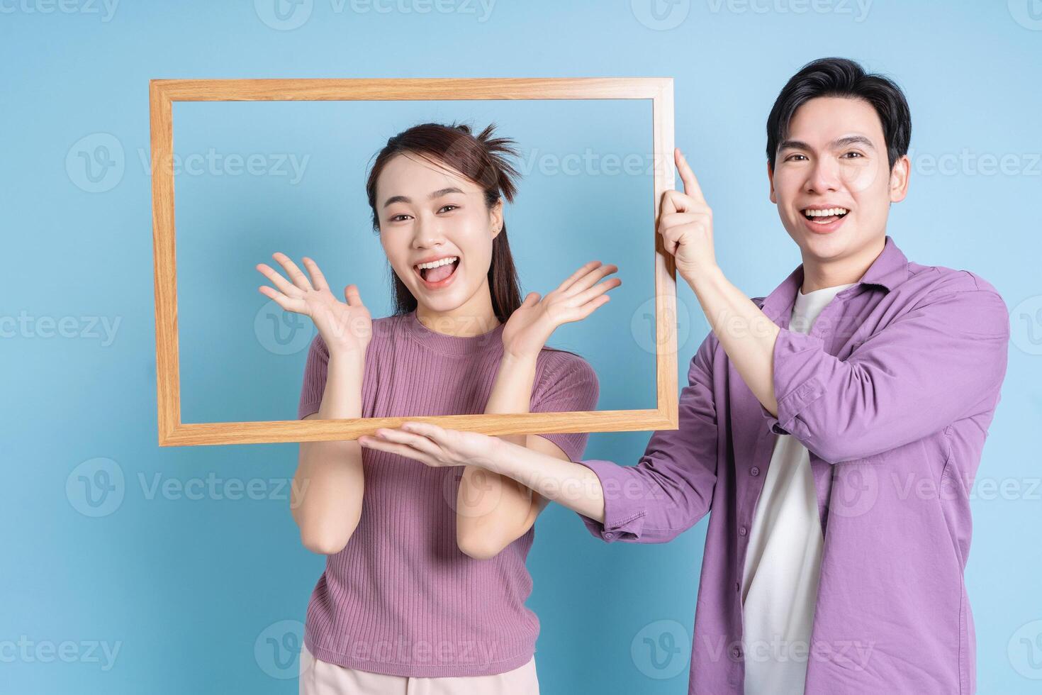 Young Asian couple holding photo frame on blue background