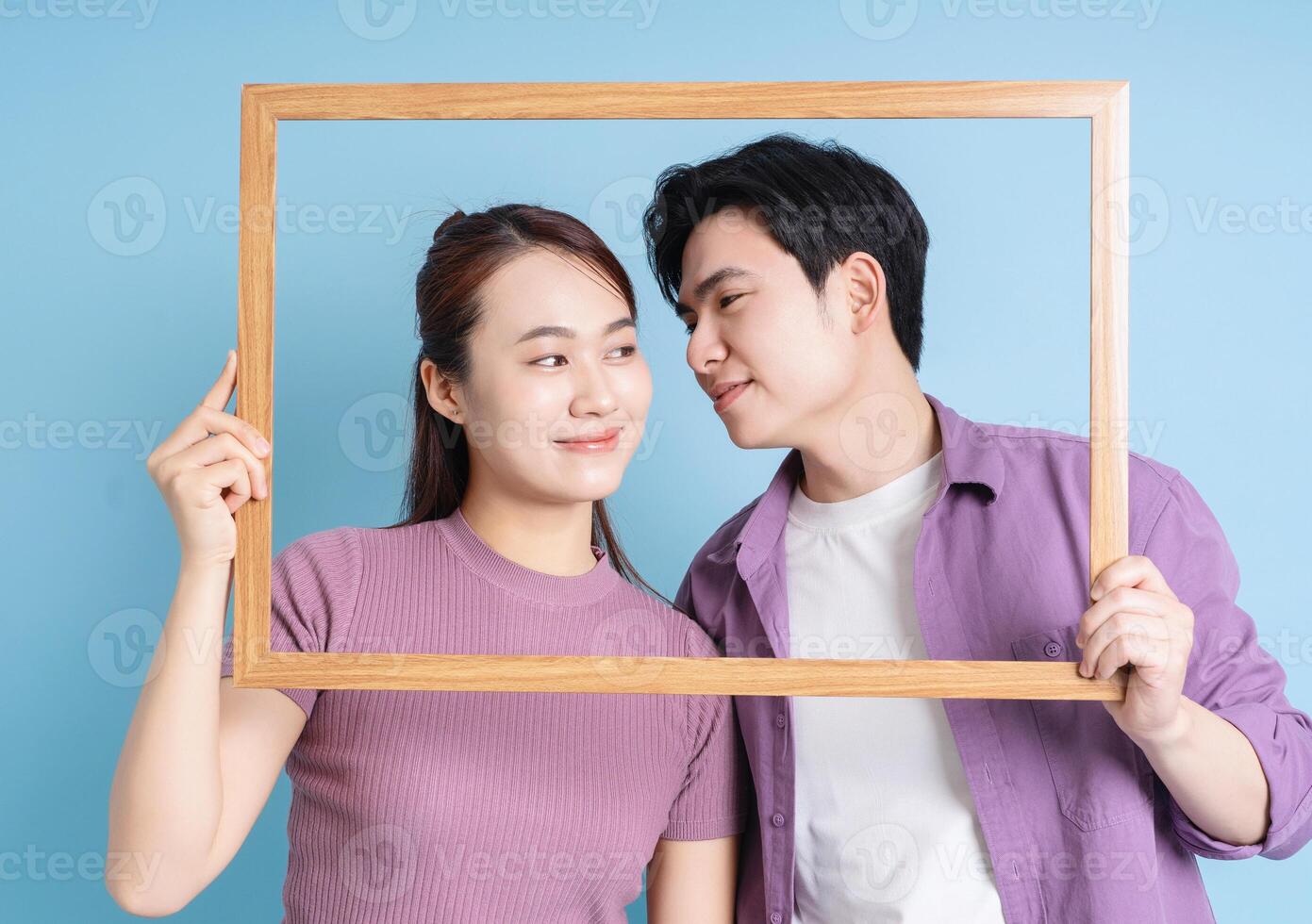 Young Asian couple holding photo frame on blue background