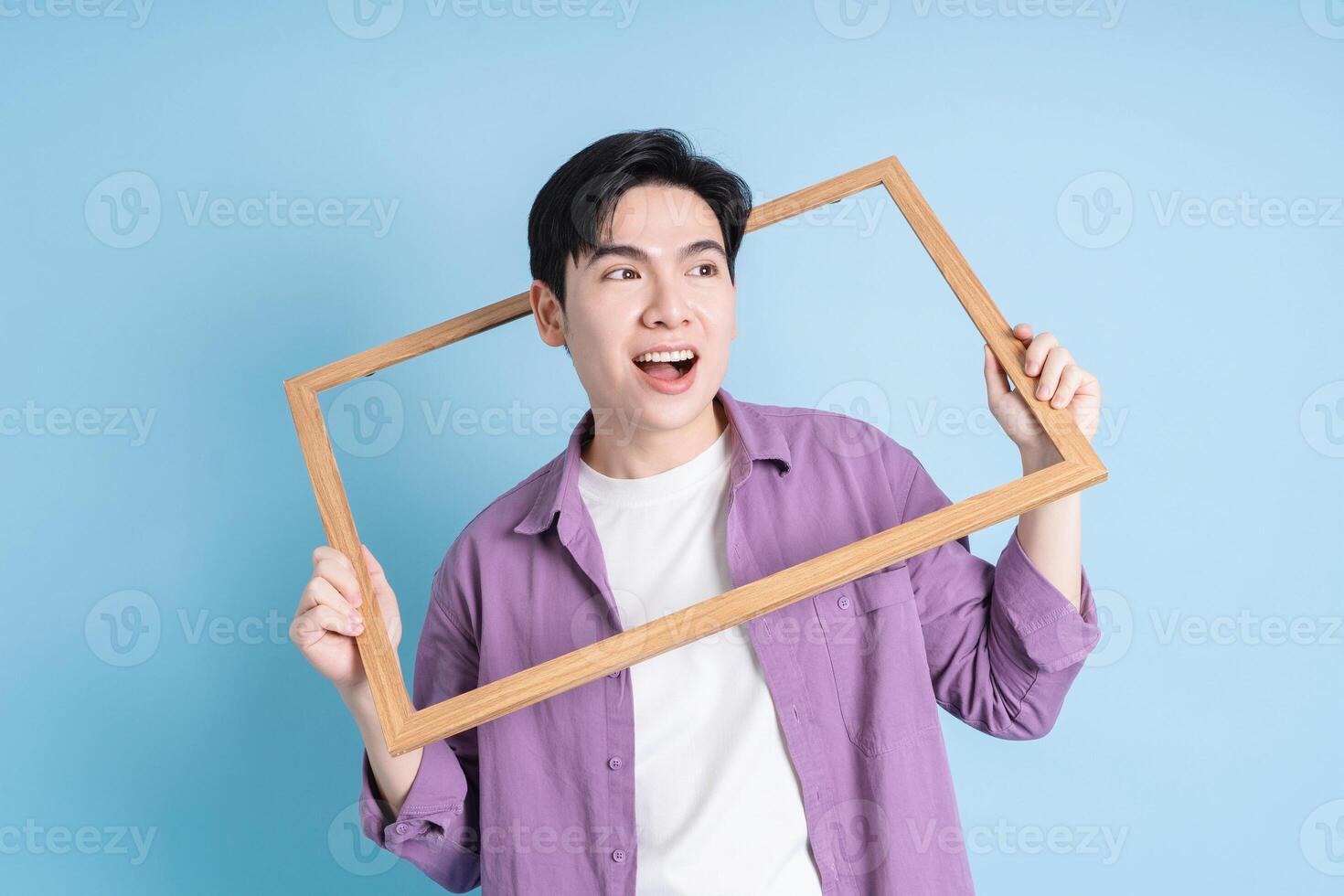 Young Asian man holding photo frame on blue background