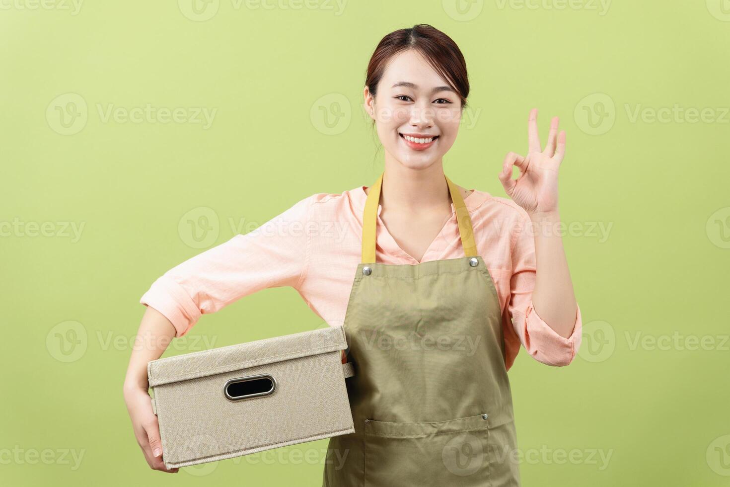 Photo of young Asian female housekeeper on green background