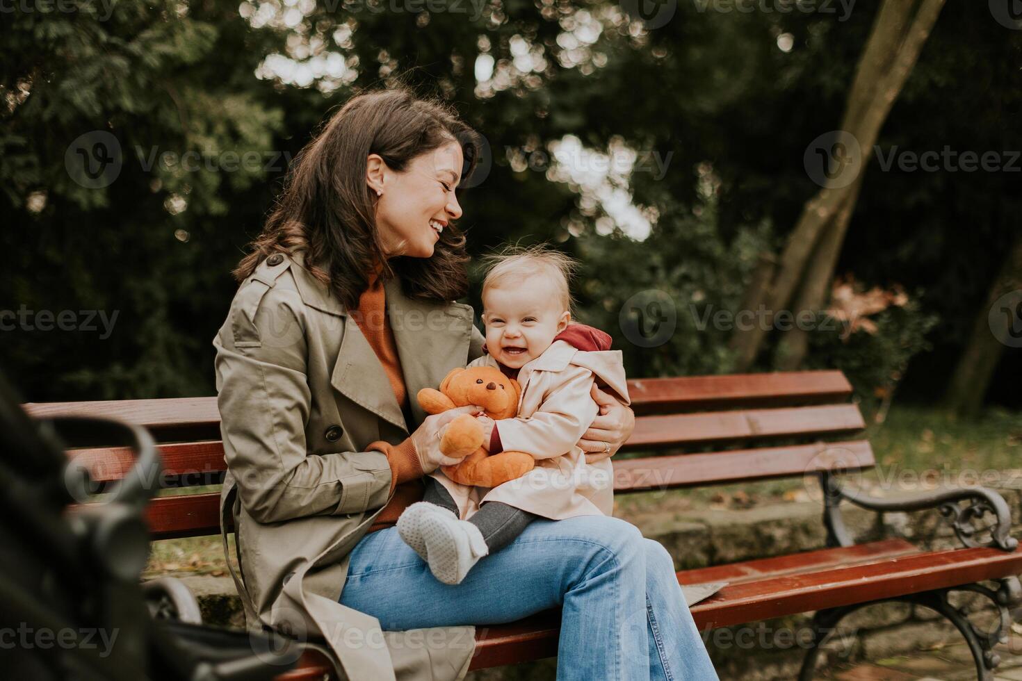 Young woman sitting on a bench with cute baby girl in the autumn park photo