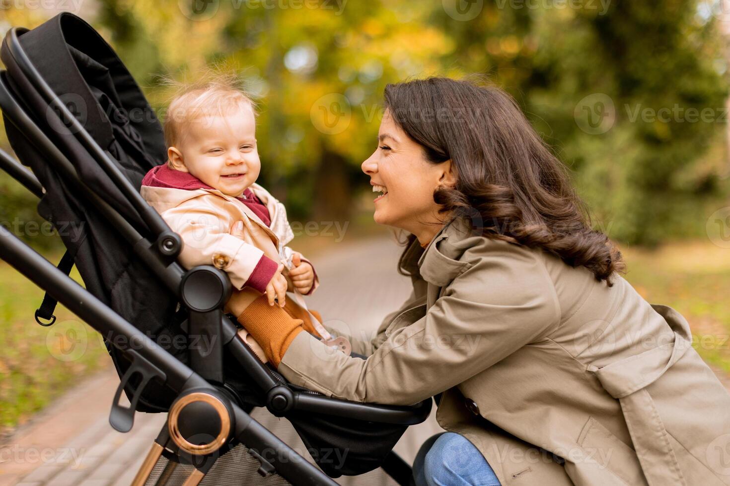 Young woman with cute baby girl in baby stroller at the autumn park photo