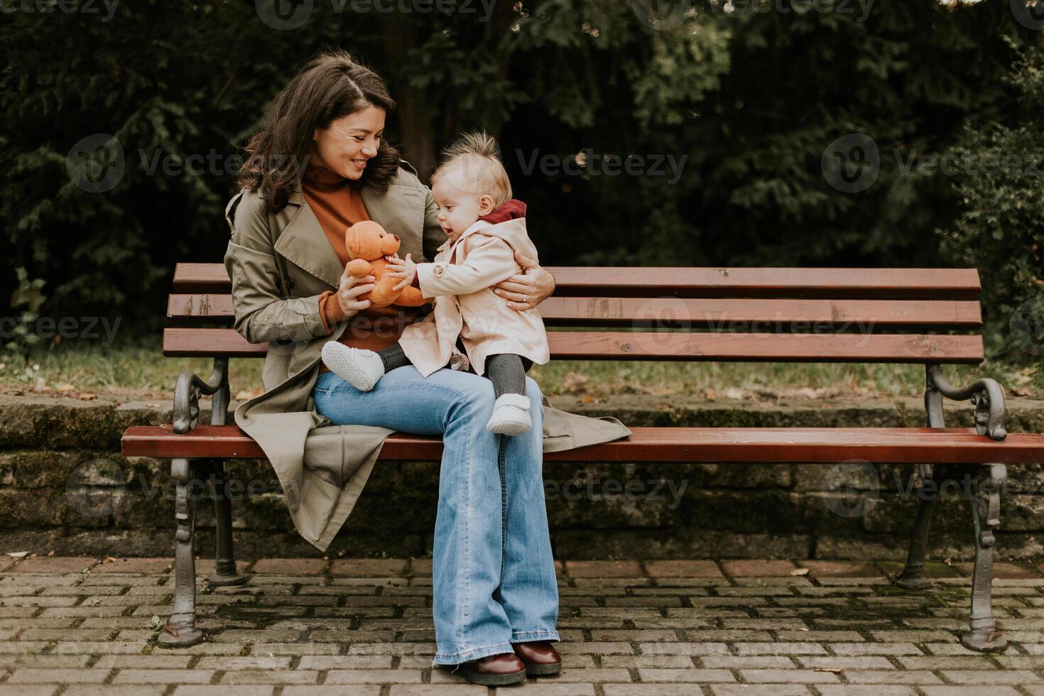 Young woman sitting on a bench with cute baby girl in the autumn park photo