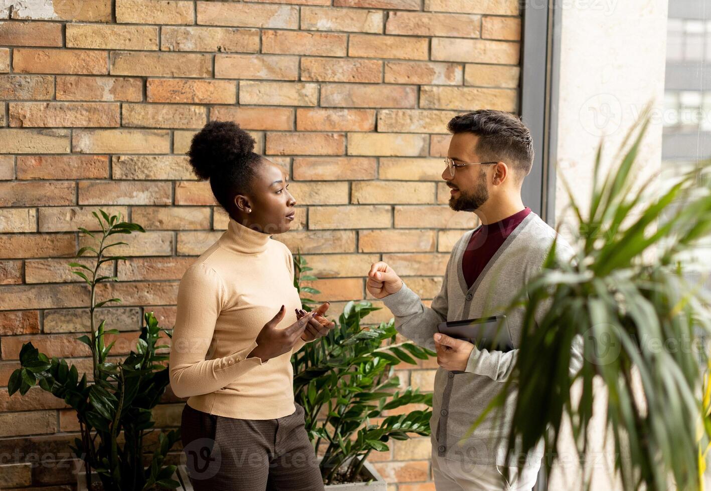 Young multiethnic business couple with digital tablet standing and discussing in the modern office photo