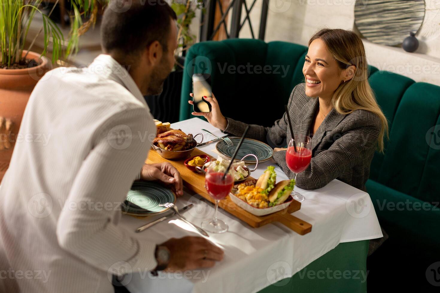 Young coupleusing mobile phone while having lunch and drinking fresh squeezed juice in the restaurant photo