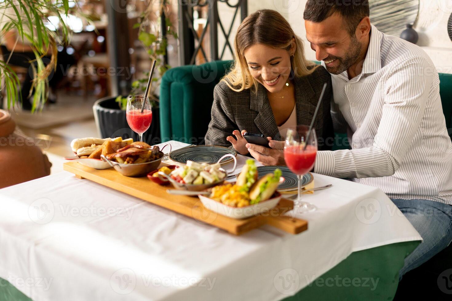 Young coupleusing mobile phone while having lunch and drinking fresh squeezed juice in the restaurant photo
