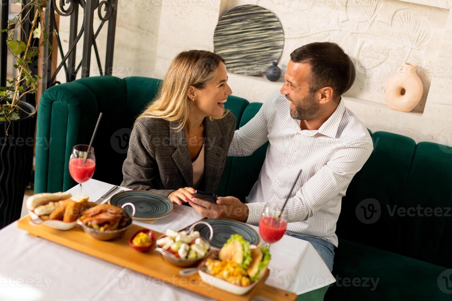 Young coupleusing mobile phone while having lunch and drinking fresh squeezed juice in the restaurant photo