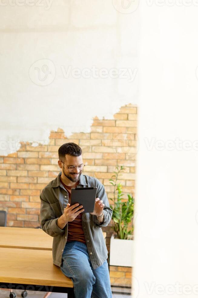 Smiling Man With Tablet in a Modern Brick-Walled Office photo