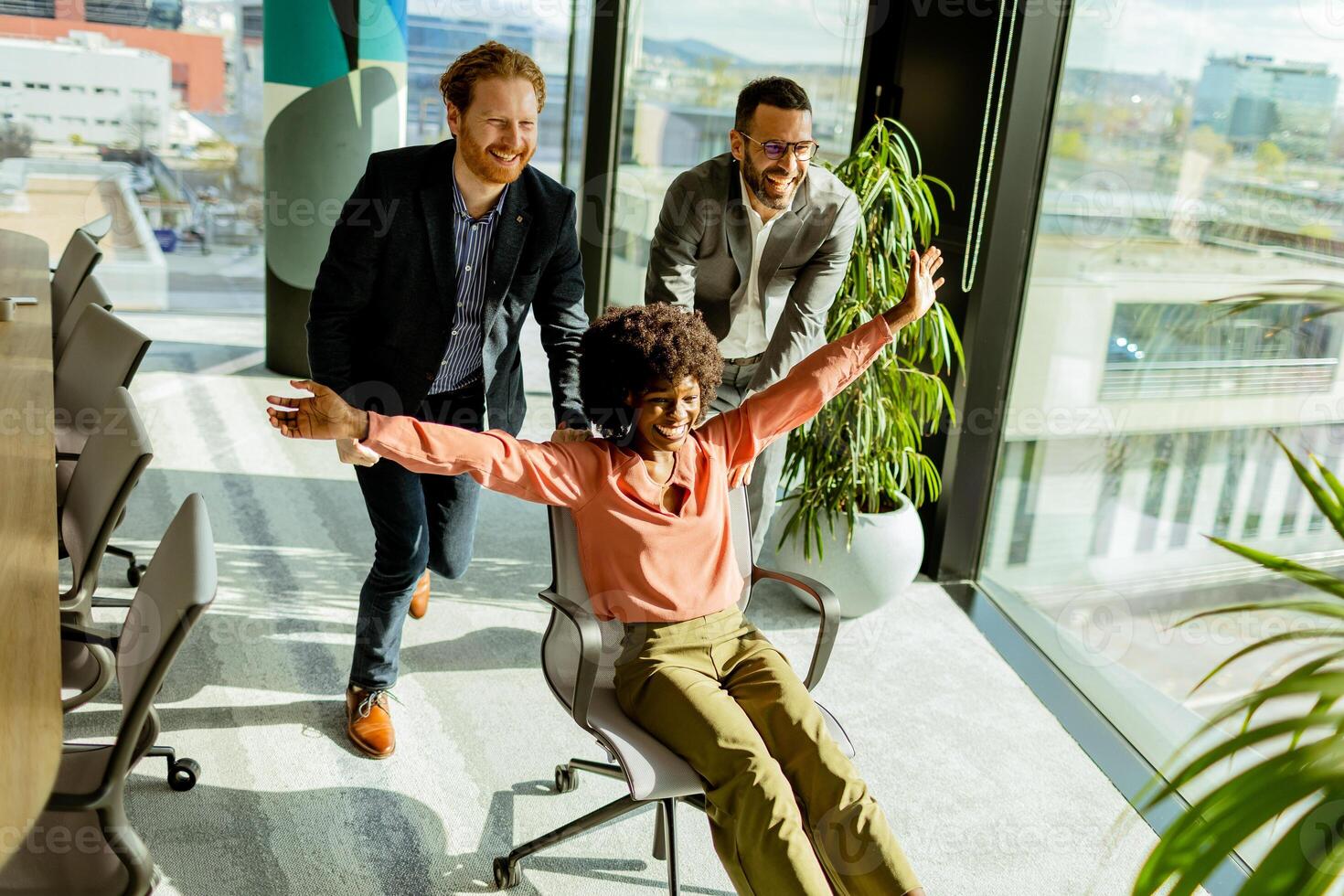 Jubilant Office Celebration Captures Colleagues Spontaneous Chair Race in Sunlit Room photo