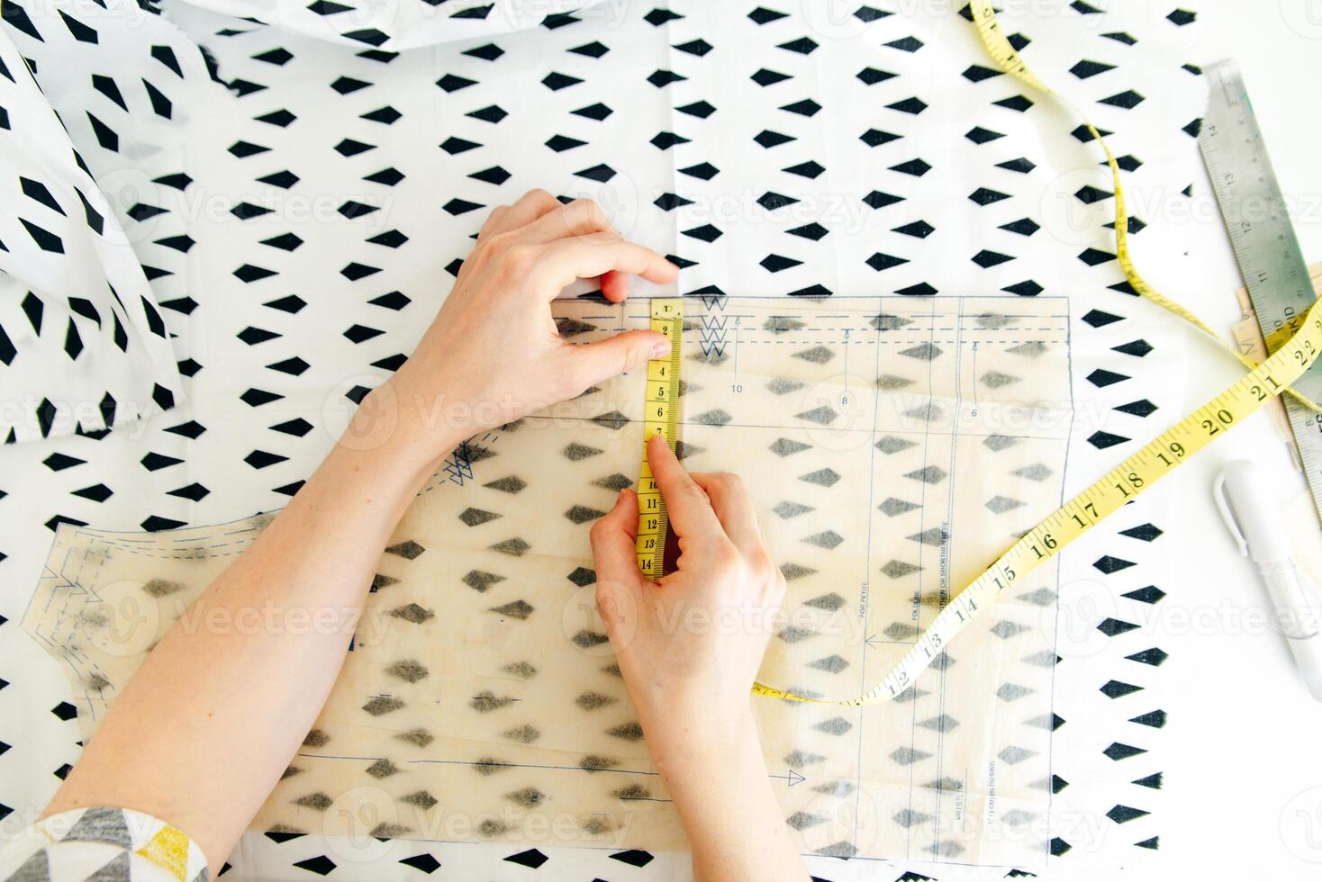 Top view of workplace of seamstress. Dressmaker cuts detail on sketch. Seamstress cuts pink fabric with scissors. photo