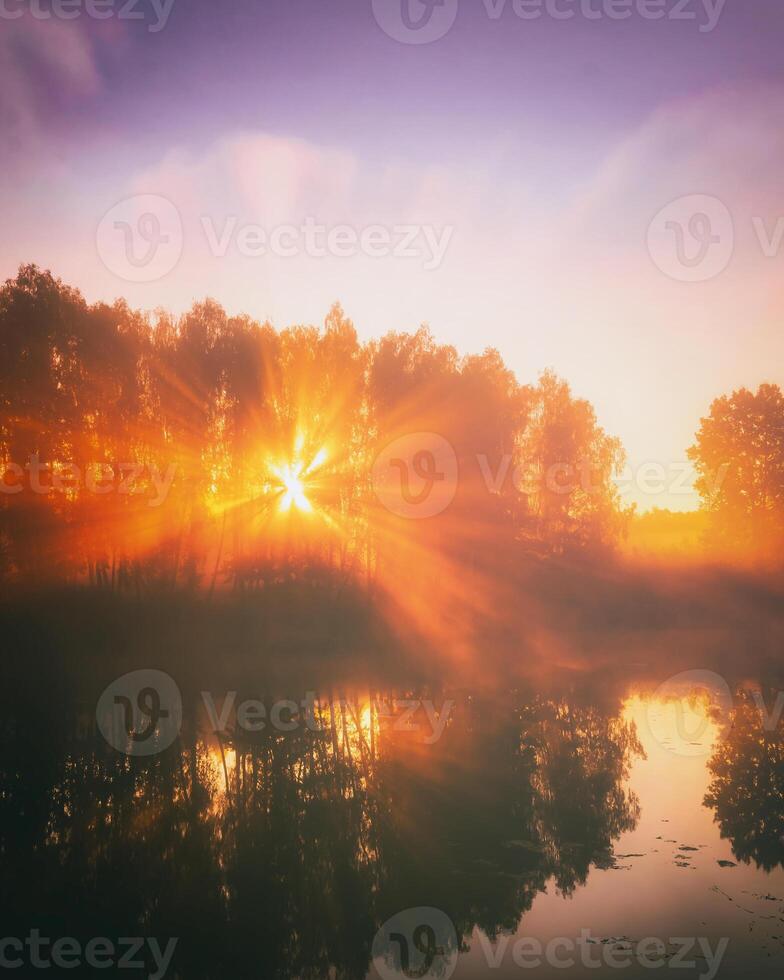 Dawn on a lake or river with a sky reflected in the water, birch trees on the shore and the sunbeams breaking through them and fog in autumn. Aesthetics of vintage film. photo