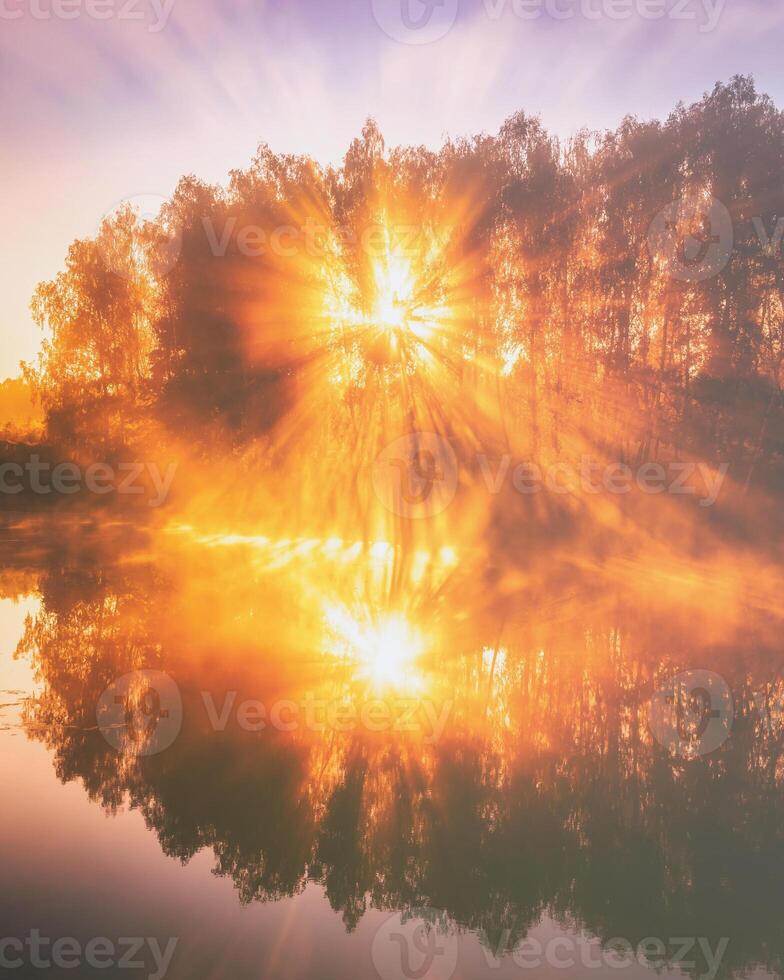 Dawn on a lake or river with a sky reflected in the water, birch trees on the shore and the sunbeams breaking through them and fog in autumn. Aesthetics of vintage film. photo