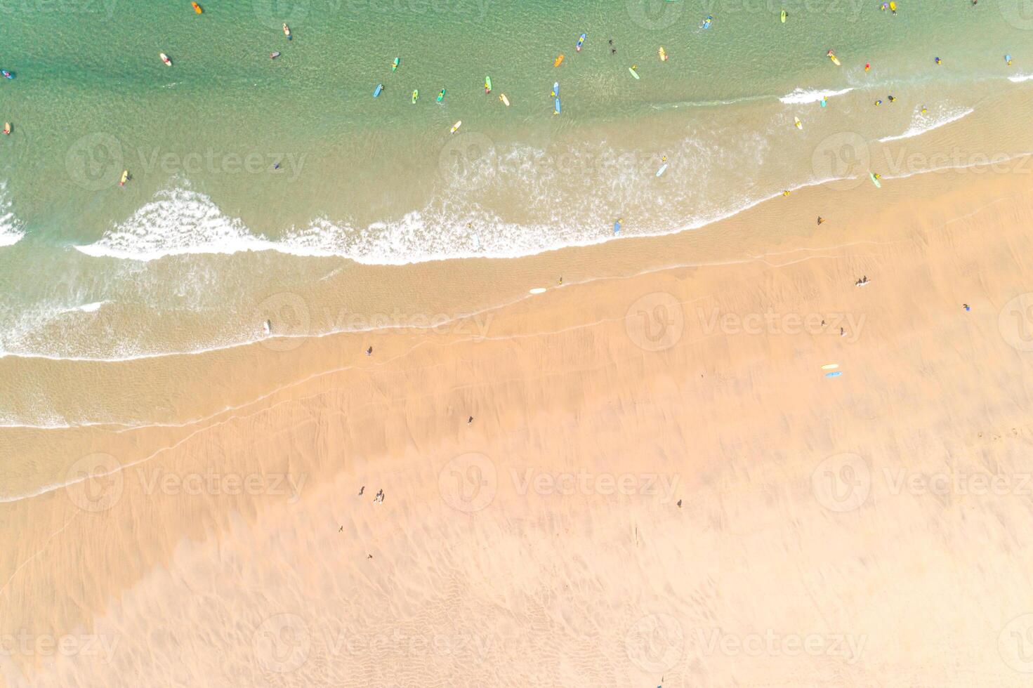 aerial drone top view of a beach, people walking on the sand and surfers with their surfboards in the turquoise water. photo