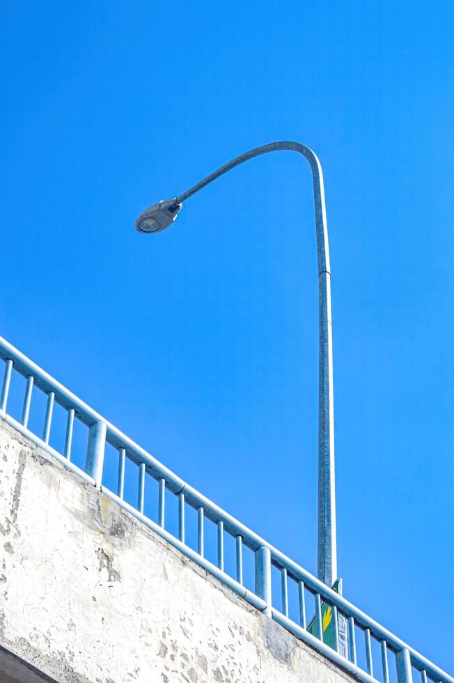 a street lamp on the side of the road above the fly over bridge from the viewpoint of the lower part of the bridge against a bright blue sky background photo
