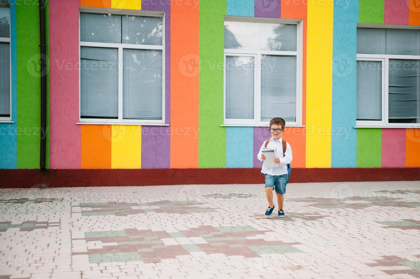 Back to school. Happy smiling boy in glasses is going to school for the first time. Child with backpack and book outdoors. Beginning of lessons. First day of fall. photo