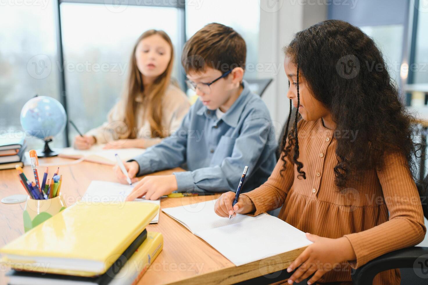 Focused multiracial students kids writing down data into notebook while sitting at table photo