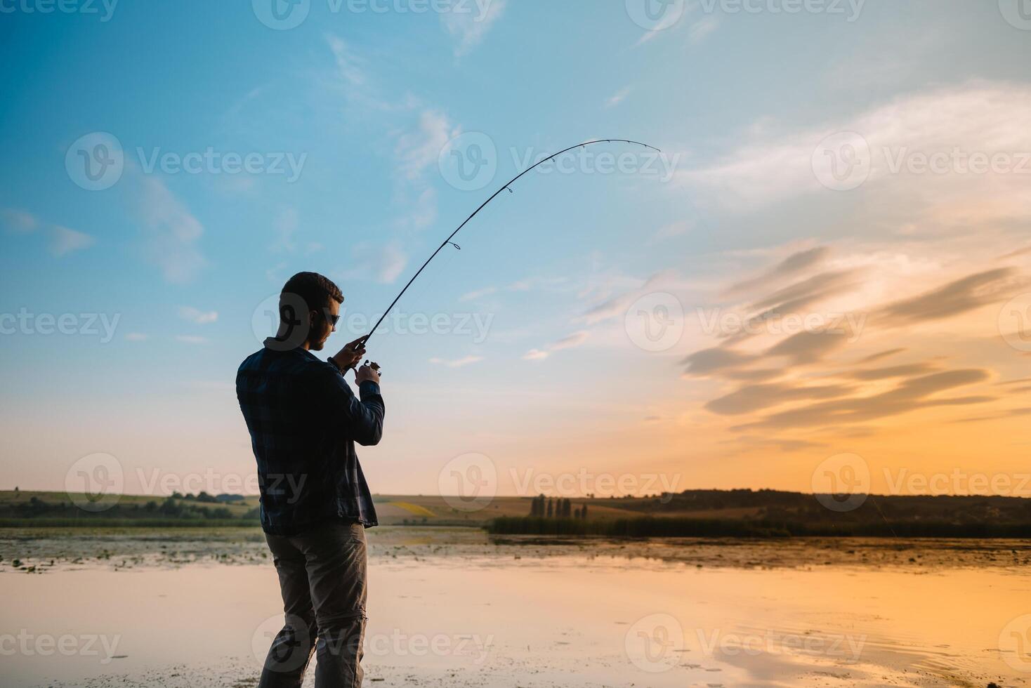 Fisherman at sunset on the river .Beautiful summer landscape with sunset on the river. Fishing. spinning at sunset. Silhouette of a fisherman. photo