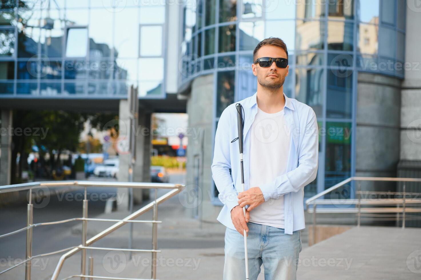 Young handsome blinded man walking with stick in town photo
