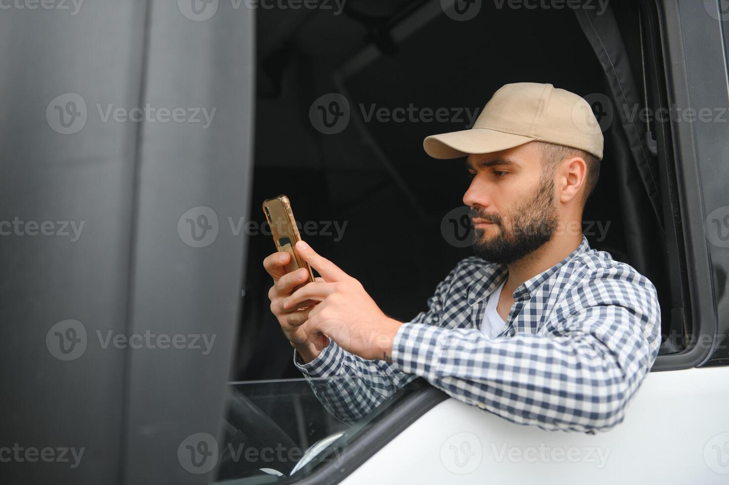 A driver sitting inside the semi-truck while looking through the open window with multiple trucks parked in the background photo