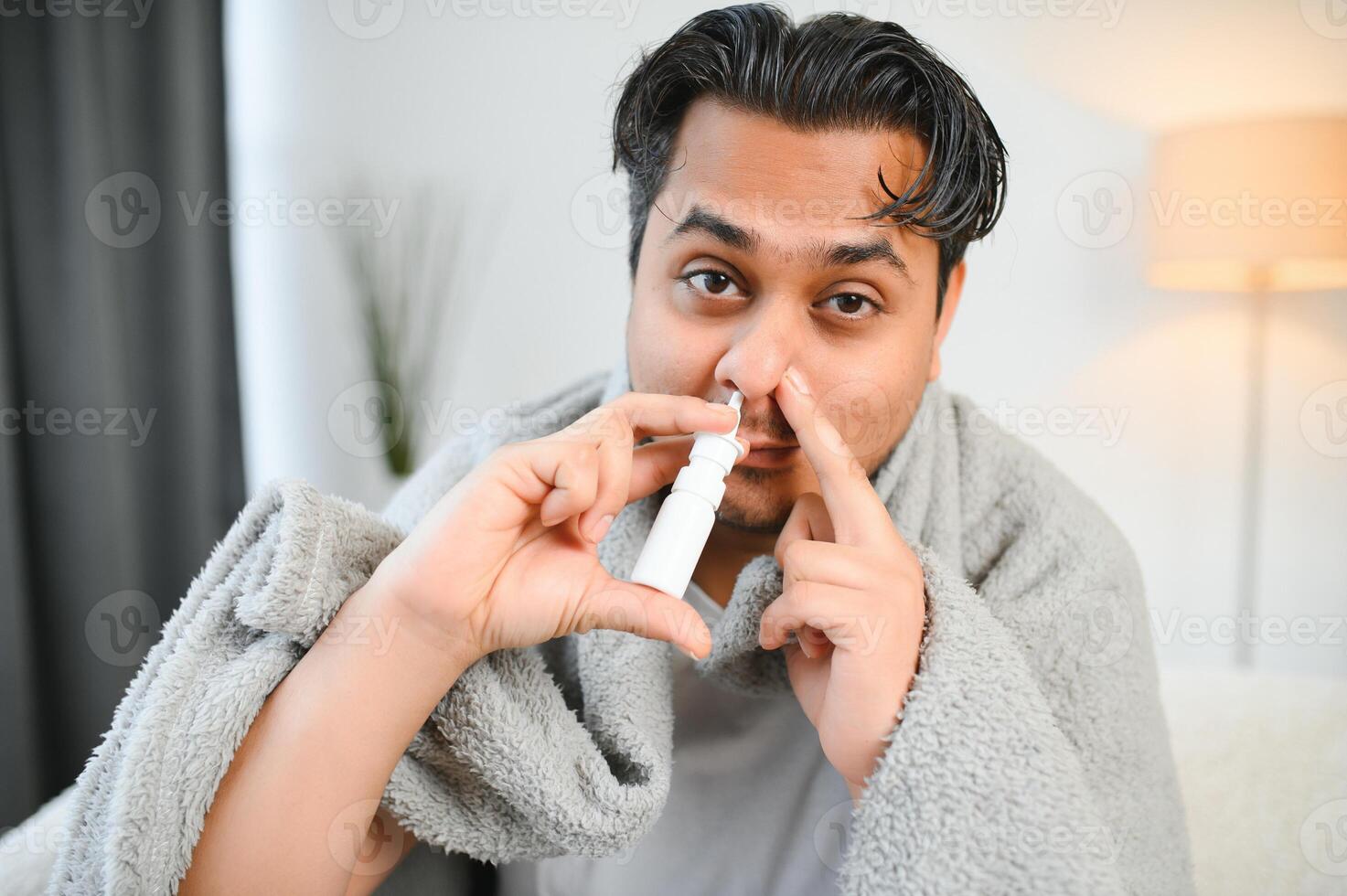 A sick Indian is treated at home and uses a nasal spray. Healthcare concept photo