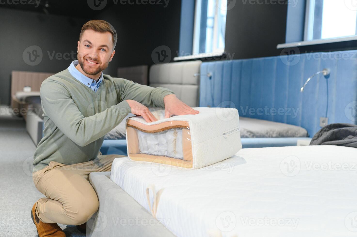 Young male customer examining orthopedic mattress on sale at furniture store, copy space photo
