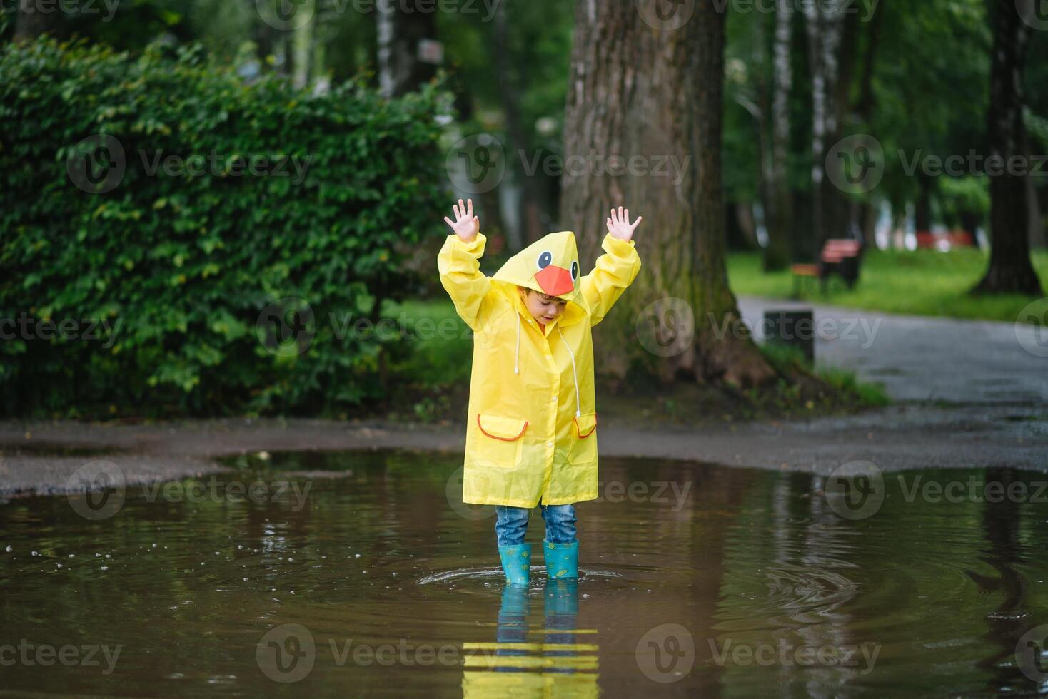 pequeño chico jugando en lluvioso verano parque. niño con paraguas, impermeable Saco y botas saltando en charco y barro en el lluvia. niño caminando en verano lluvia al aire libre divertido por ninguna clima. contento infancia foto