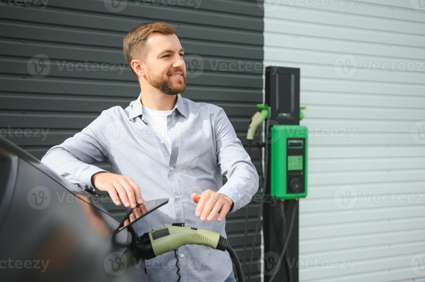 A man stands near a charging station and charges his electric car photo